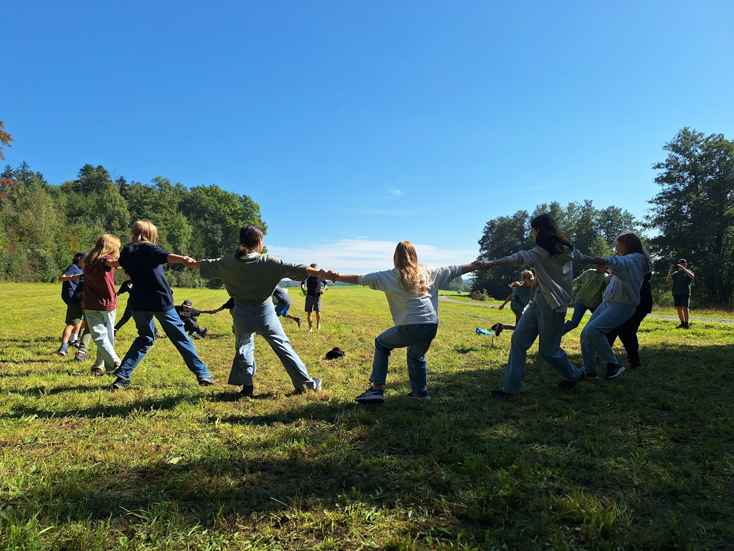 Ryhmä ihmisiä pitämässä toisiaan kädestä kiinni kävellessään ruohoisella pellolla.